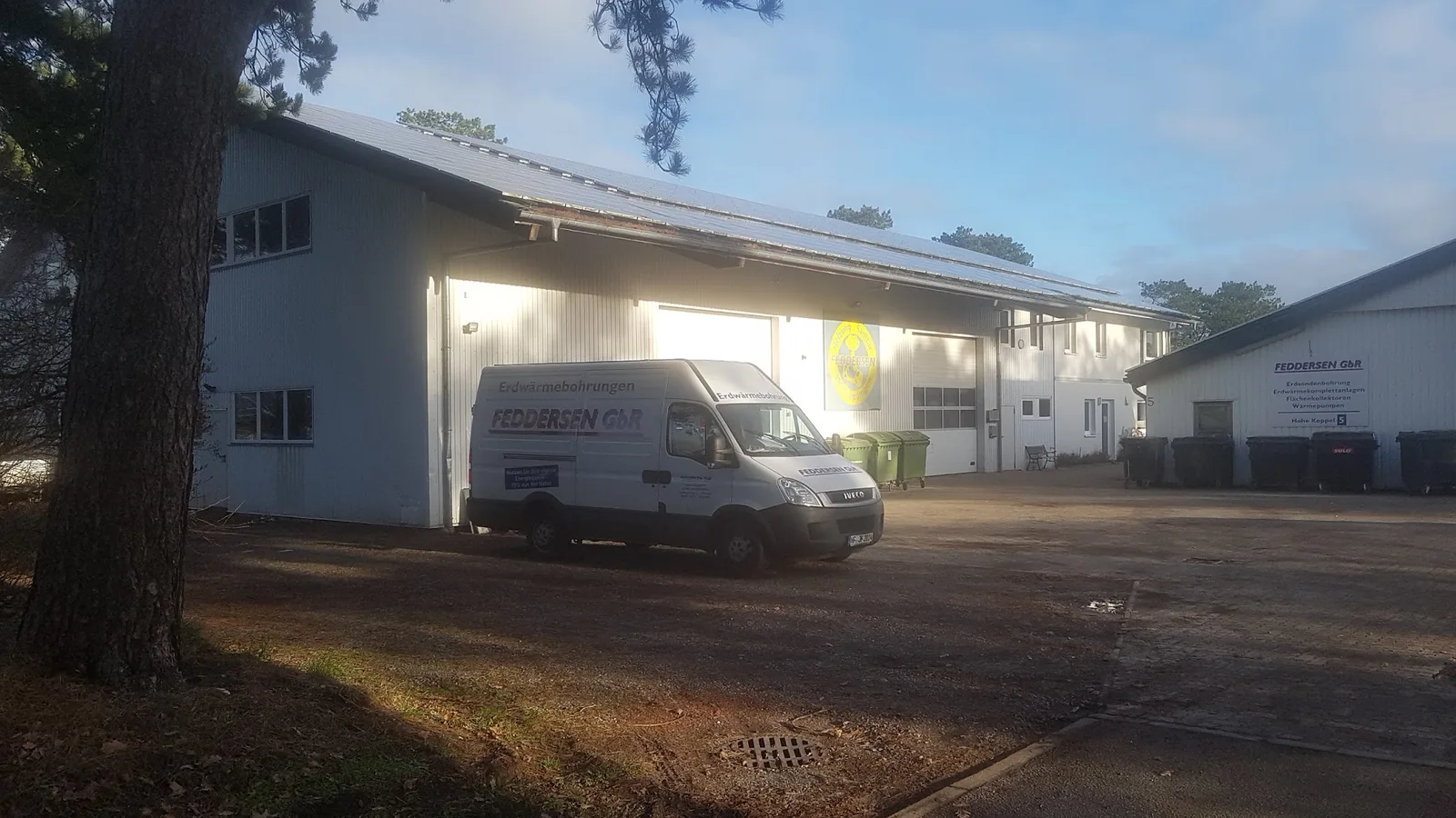 Halle mit rundem Firmenlogo, Photovoltaik auf dem Dach und Transporter auf dem Hof