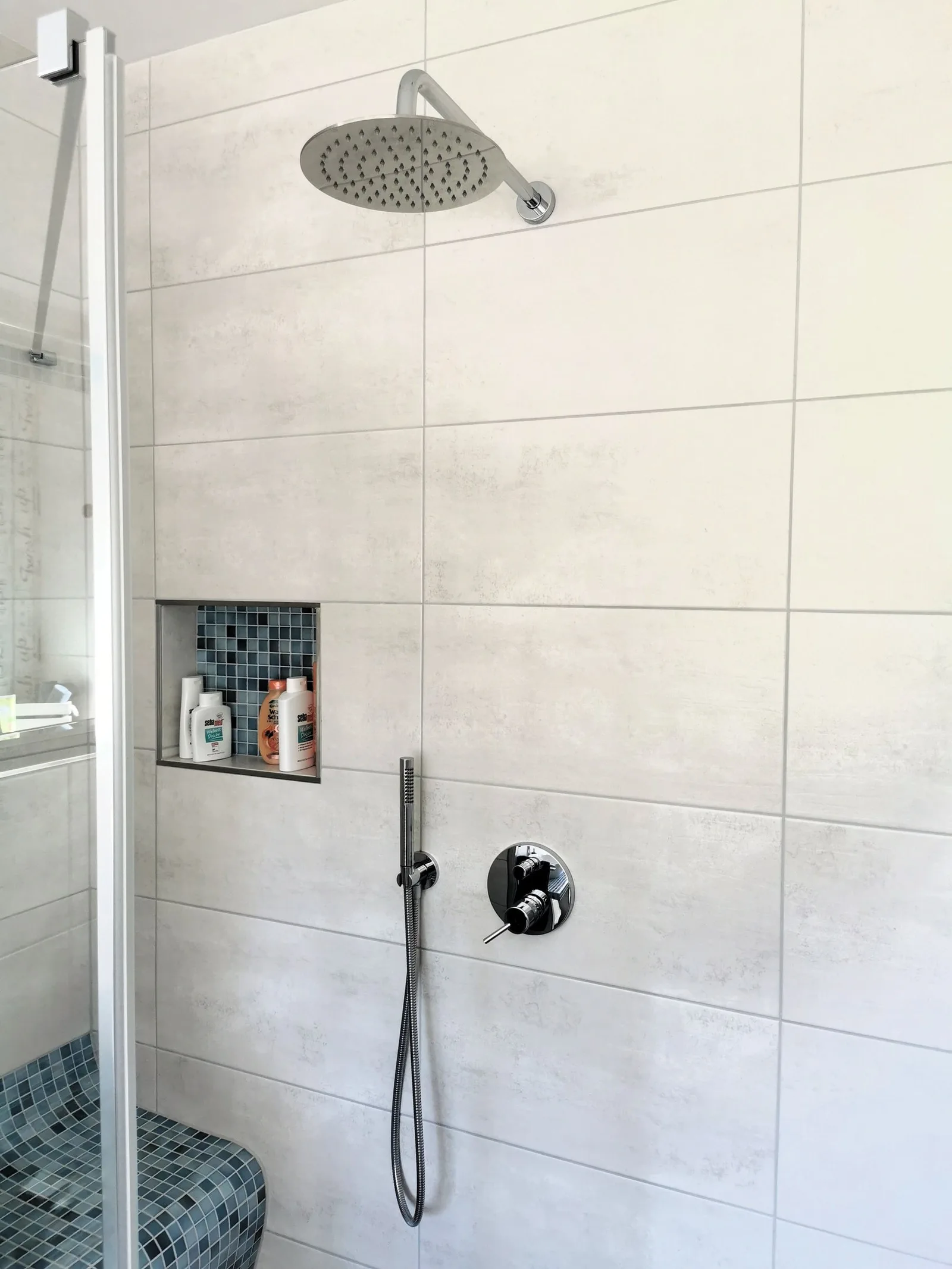 Dusche mit großer Kopfbrause und Mosaiknische in heller Fliese