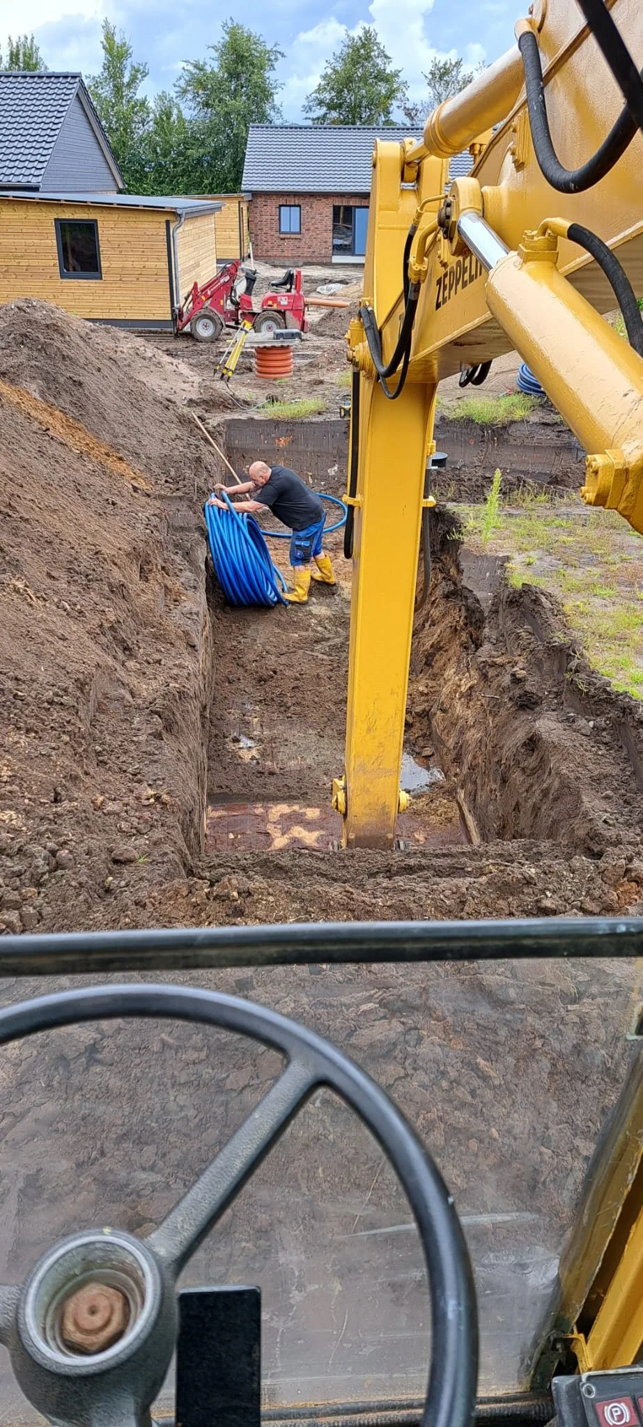 Bagger hebt einen Graben im Garten aus, im Graben blaue Rohre