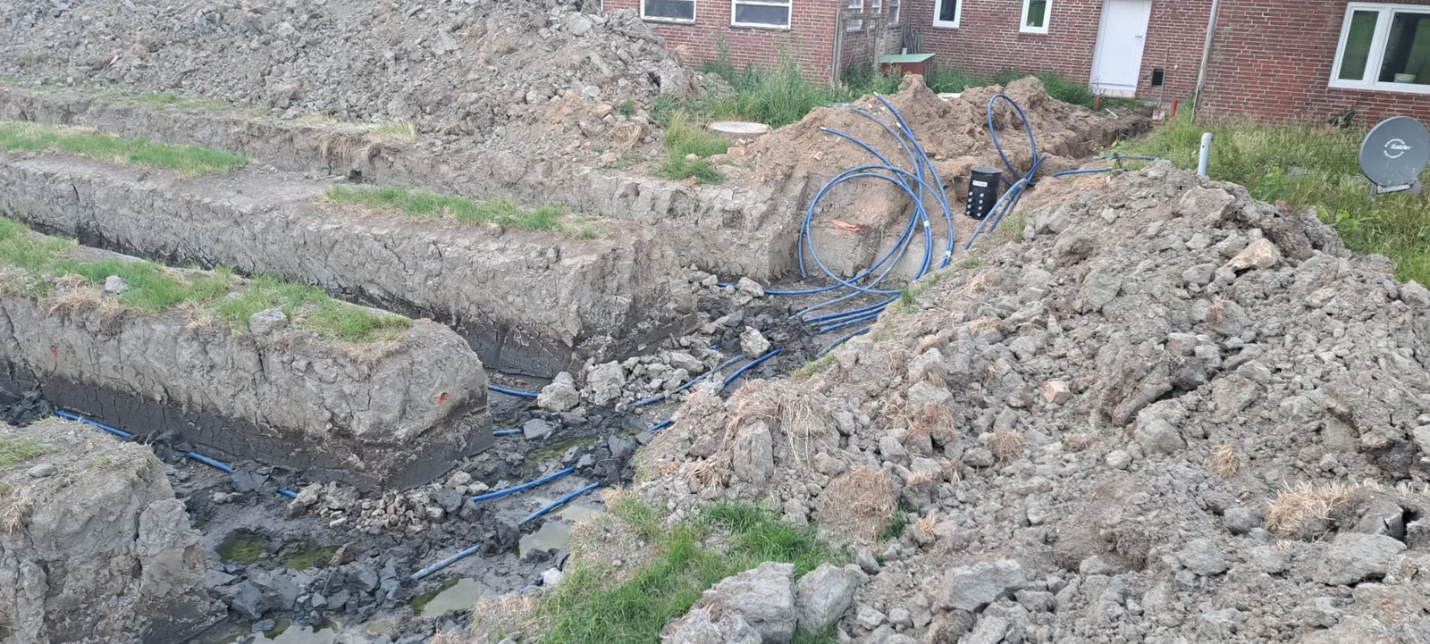 Ausgehobene Gräben mit verlegten Kollektorrohren im Garten vor einem Klinkerhaus